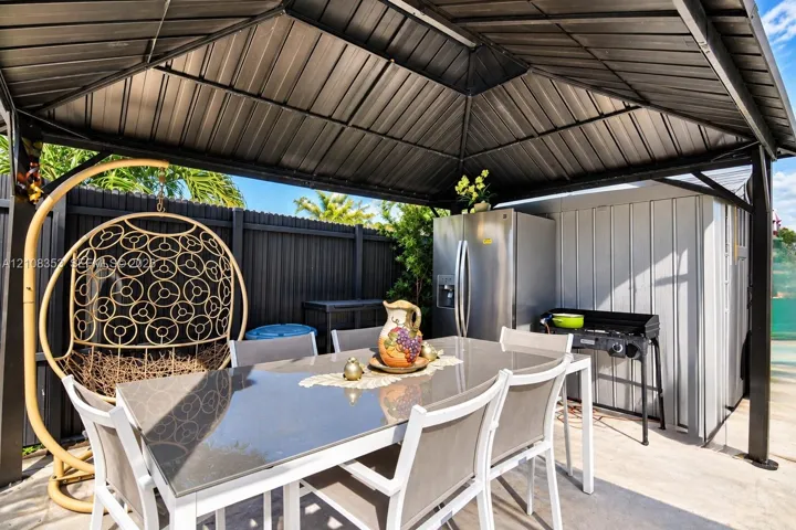 Covered outdoor pavilion featuring a dark metal roof, concrete flooring, and a corrugated privacy fence
