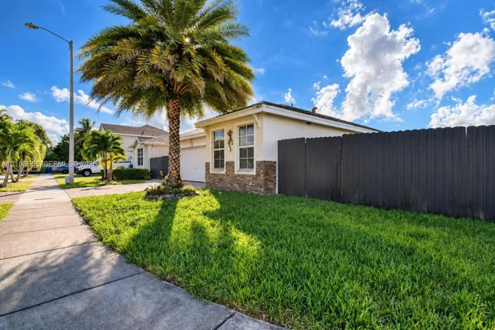Exterior featuring a stucco facade with stone veneer accents, multi-pane windows, a dark privacy fence, and a palm tree within a grass lawn