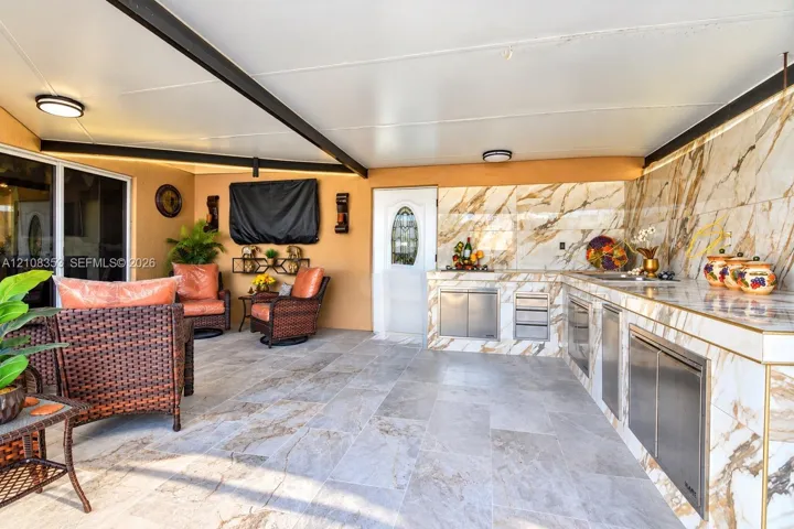 Covered outdoor kitchen featuring stone-clad countertops and backsplash, stainless steel cabinetry, tile flooring, and integrated ceiling lighting