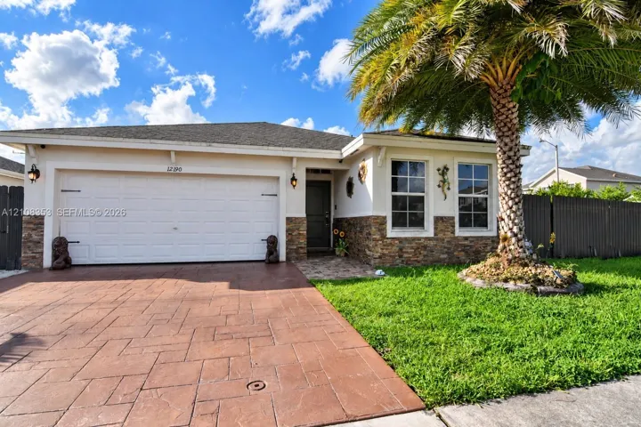 Single-story exterior featuring a stone veneer facade, a stamped concrete driveway, a dual-car garage, and a manicured front lawn with a mature palm tree