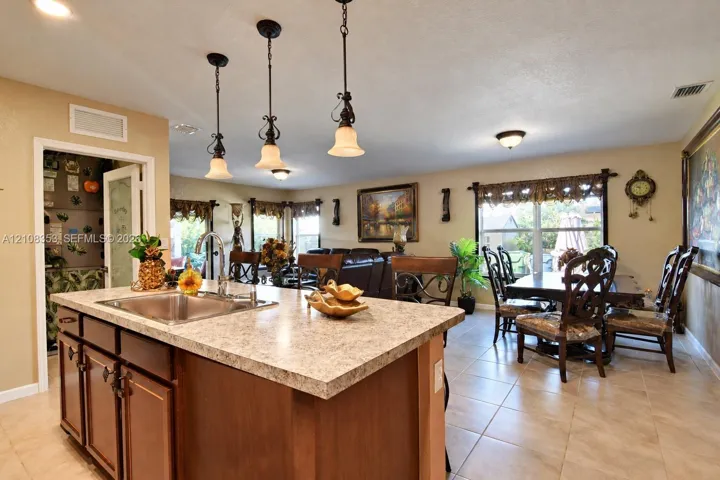 Kitchen featuring a center island with a stone-finish countertop and integrated sink, medium-toned wood cabinetry, tile flooring, and three industrial-style pendant light fixtures