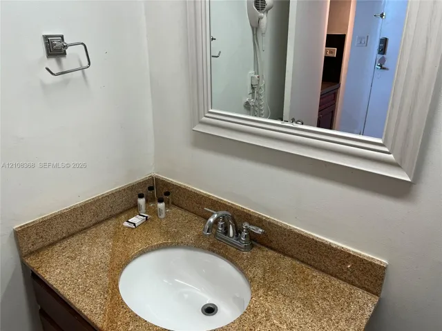 Vanity featuring a stone-composite countertop with an integrated undermount sink, chrome double-handle faucet, and a wall-mounted framed mirror