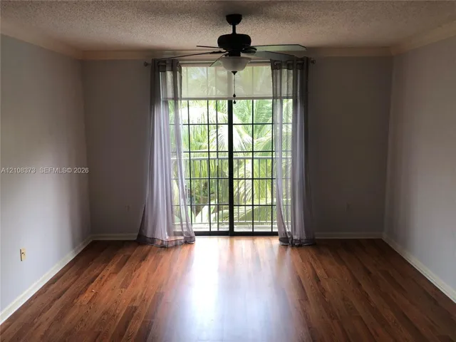 Wood-finish flooring, ceiling fan with integrated light fixture, and black-framed sliding glass doors opening to an exterior railing