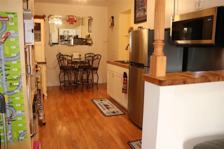 Kitchen featuring stainless steel appliances, wood-finish flooring, white cabinetry, and a wood-topped peninsula with a decorative post