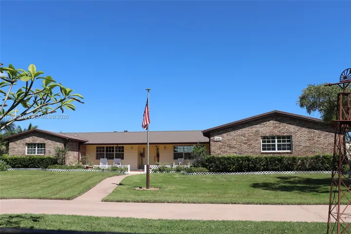 Single-story brick exterior featuring a metal roof, front covered porch, manicured lawn, and ornamental windmill structure
