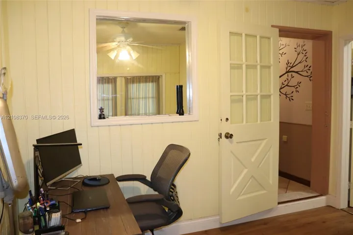 Vertical wood-panel walls, interior fixed-pane window, nine-pane glass and wood door with cross-buck paneling, and wood-finish flooring