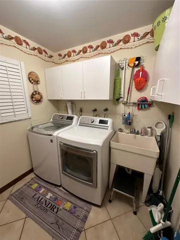 Laundry area featuring white cabinetry, a freestanding utility sink with faucet, ceramic tile flooring, and plantation shutter window coverings