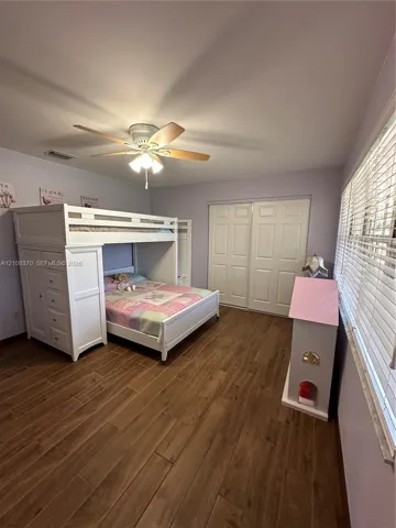 Wood-finish plank flooring, ceiling fan with integrated light fixture, and dual-panel sliding closet doors
