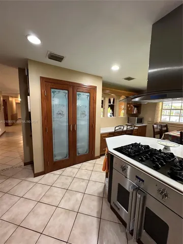 Double pantry with frosted glass paneled doors, stainless steel gas range with overhead ventilation hood, recessed lighting, and tile flooring