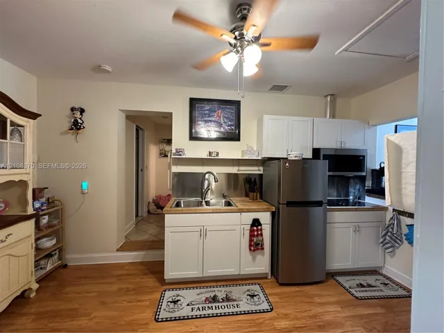 Kitchen featuring white shaker-style cabinetry, wood-finish countertops, a stainless steel undermount sink with a gooseneck faucet, stainless steel appliances, and wood-finish flooring