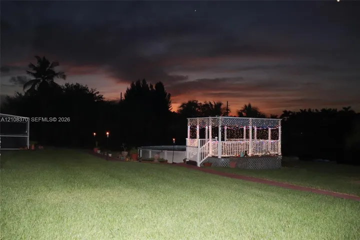 Backyard area featuring an elevated wooden gazebo, an above-ground pool, and a manicured lawn