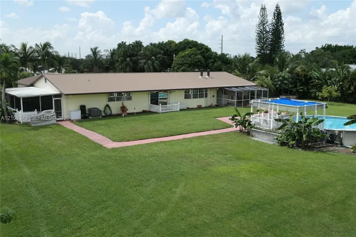 Expansive backyard featuring a manicured lawn, inground swimming pool with a pergola, screened-in porch, and concrete paver walkways