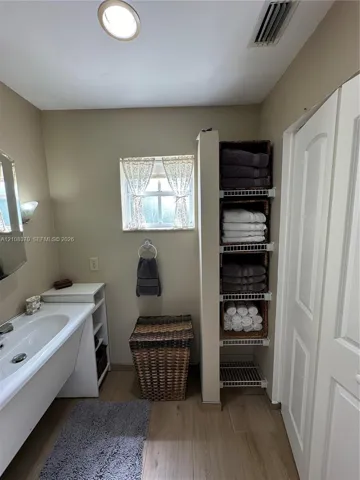 Bathroom featuring a vanity with an integrated sink, built-in wire shelving, wood-finish flooring, and a window with a sash lock