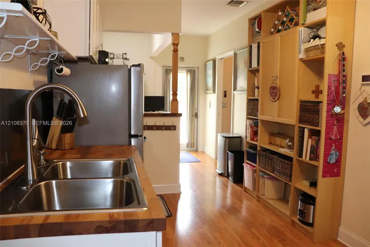Kitchen featuring a butcher block countertop, stainless steel dual-basin sink with a high-arch faucet, wood-finish flooring, and floor-to-ceiling built-in cabinetry