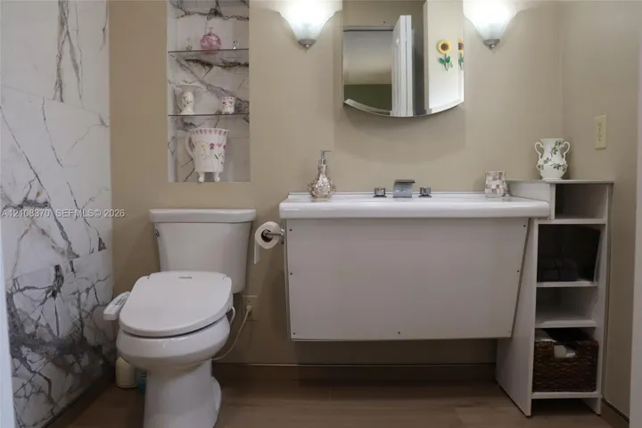 Wall-mounted sink with integrated storage, full-height stone-patterned tile wall, recessed shelving, and dual wall-mounted light fixtures
