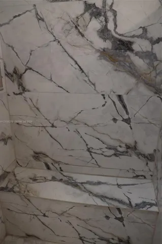 Shower enclosure featuring large-format veined stone wall tile and a built-in stone bench