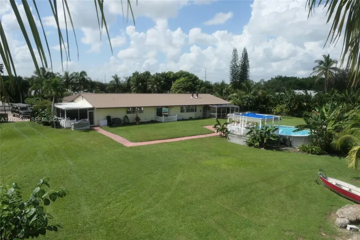 Expansive backyard featuring a large grass lawn, screened-in patio, and an above-ground swimming pool with a hardscape surround