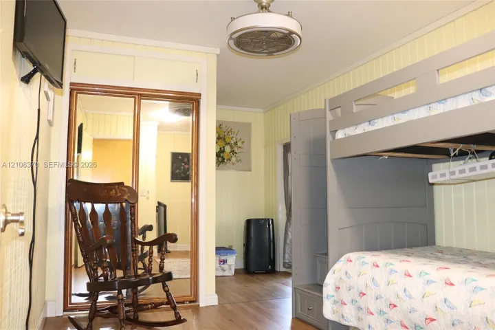 Wood-finish flooring, vertical panel wall detailing, mirrored sliding closet doors with built-in overhead storage, and a ceiling-mounted light fixture