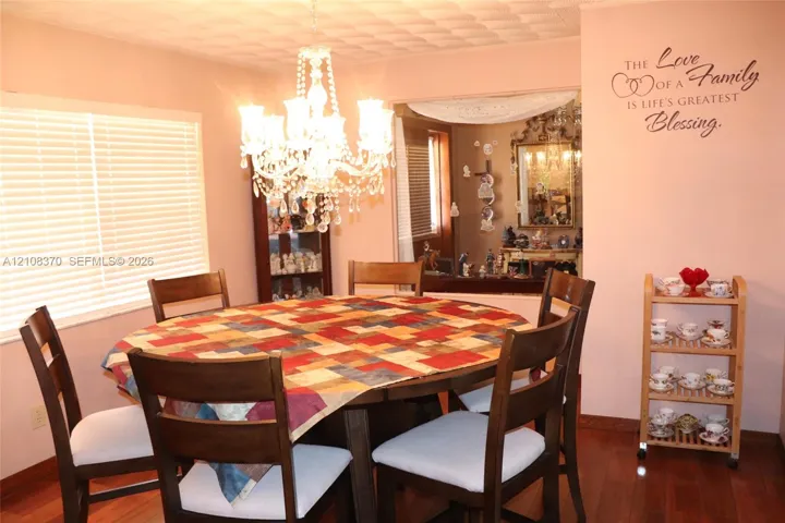 Dining area featuring wood-finish flooring, a multi-tiered crystal chandelier, and large window with horizontal blinds