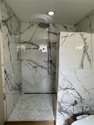 Walk-in shower featuring large-format stone-finish wall tile, hexagonal floor tiling, a rainfall showerhead, and a linear floor drain