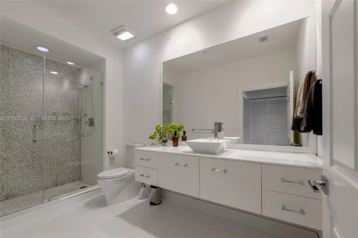 Floating white vanity with a rectangular vessel sink, solid-surface countertop, frameless glass shower enclosure, and textured stone-finish shower wall