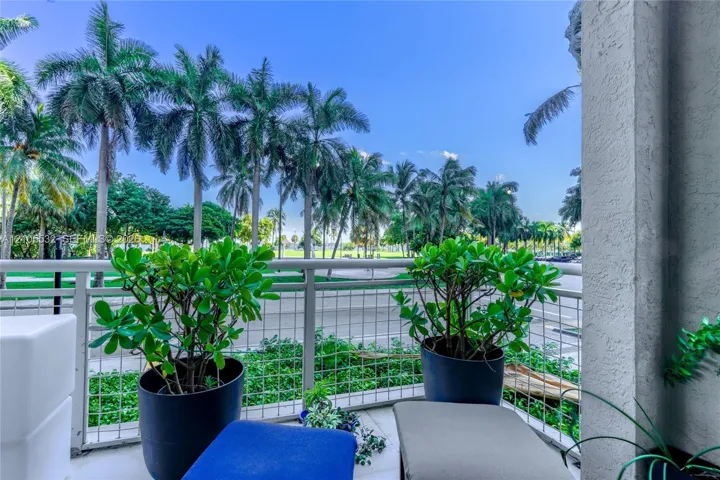 Covered balcony with white metal lattice railing, tiled flooring, and mature palm tree scenery