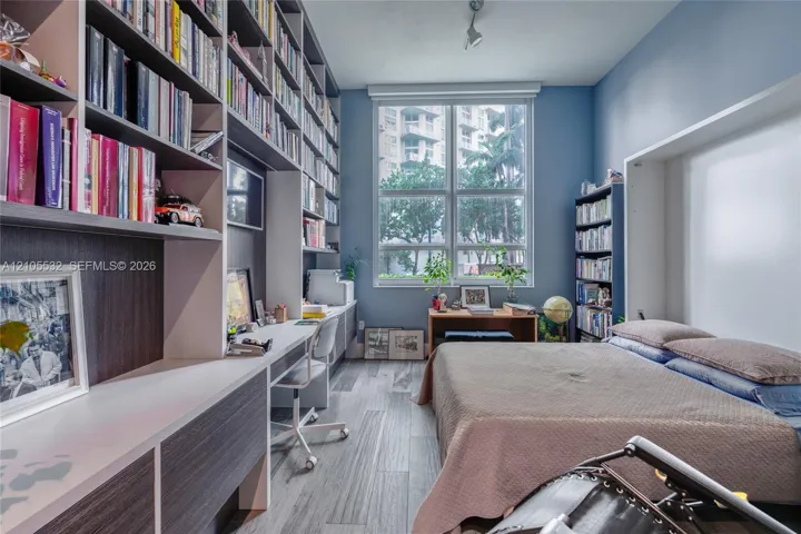 Custom floor-to-ceiling built-in shelving, integrated desk workstation, large-format window, and wood-finish flooring