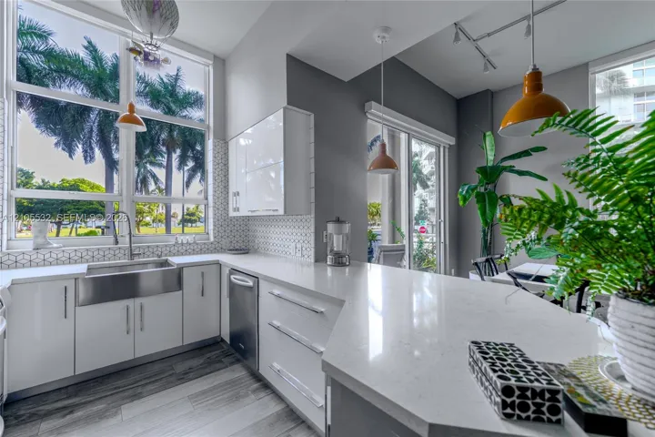 Kitchen featuring white high-gloss cabinetry, quartz countertops, a stainless steel farmhouse sink, geometric tile backsplash, and wood-finish flooring