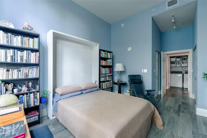 High-ceiling interior featuring a built-in Murphy bed, wood-finish flooring, and recessed ceiling lighting