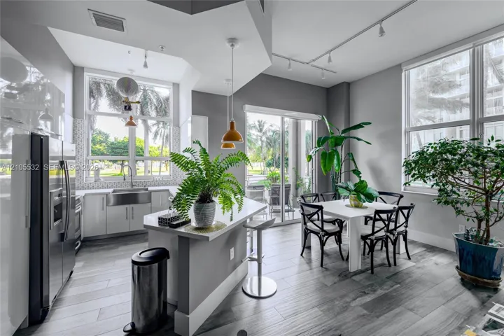 Kitchen featuring wood-finish flooring, quartz-surfaced island, stainless steel farmhouse sink, and high-reaching windows