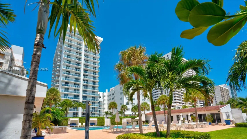 High-rise residential exterior featuring glass-railed balconies, exterior swimming pool, hardscaped patio area, mature palm trees, and manicured landscaping