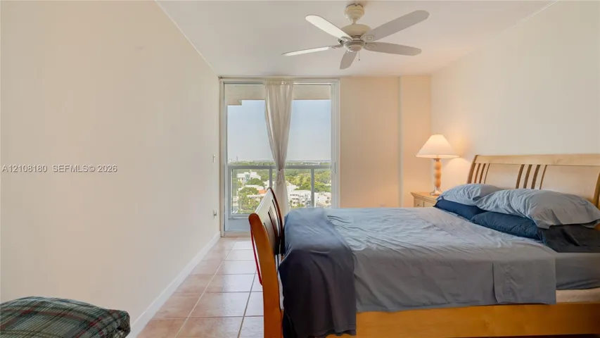 Tile flooring, ceiling fan, and large glass sliding doors leading to an exterior balcony