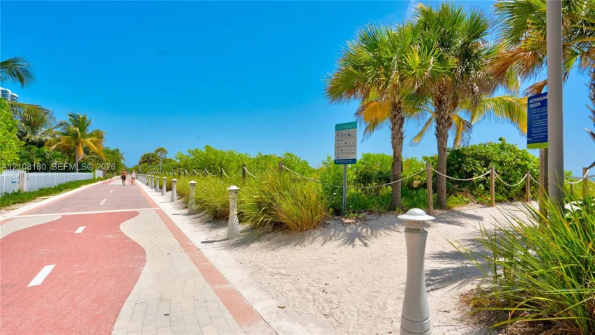 Paved multi-use trail featuring a brick-paver border, rope-fenced pathways, native landscaping, and mature palm trees