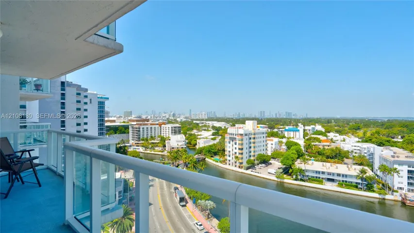 Covered balcony with a white metal railing and glass panel inserts, providing an exterior perspective of the canal and urban skyline