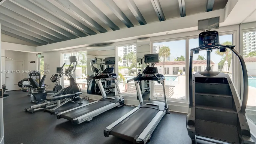 Fitness center featuring a vaulted ceiling with exposed beams, wall-to-wall mirrors, and floor-to-ceiling windows