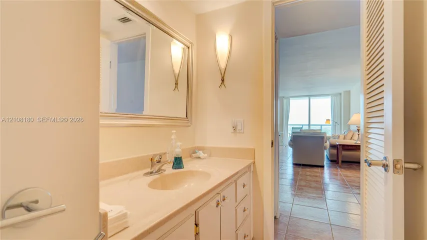 Vanity with integrated sink and countertop, framed wall mirror, dual wall-mounted sconces, and louvered-style closet door