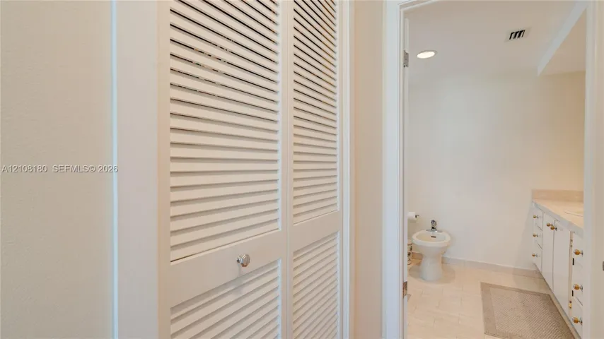 White louvered bifold closet doors featuring polished hardware, integrated white cabinetry with flat-panel drawers, and tile flooring