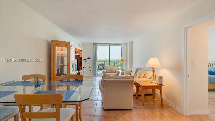 Open-concept interior featuring neutral wall tones, large-format tile flooring, and floor-to-ceiling glass doors leading to a private balcony