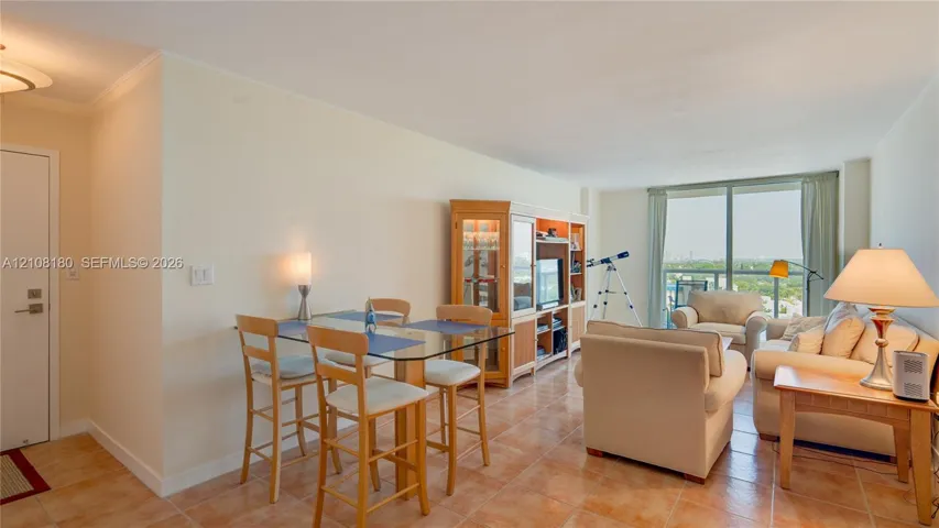 Open-concept interior featuring neutral wall tones, ceramic tile flooring, built-in wooden cabinetry, and floor-to-ceiling glass sliding doors leading to a private balcony