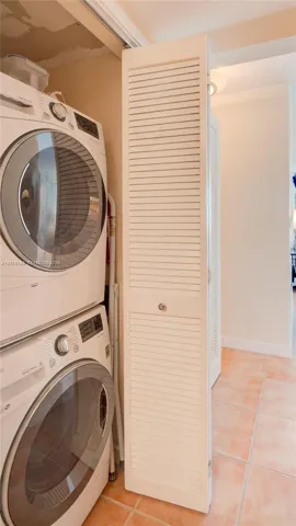 Laundry area featuring stacked appliances enclosed by a white louvered bifold door and tile flooring