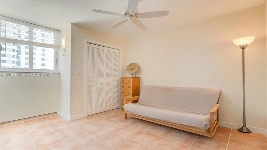 Second bedroom with ceramic tile flooring, white louvered-door closet, ceiling fan with integrated lighting, and wall-mounted sconce