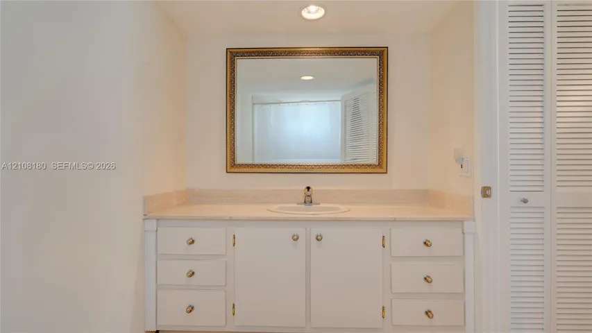 Vanity featuring a stone countertop, integrated sink, white cabinetry with metallic hardware, and a framed wall-mounted mirror