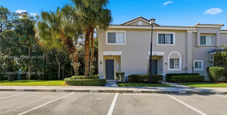 Two-story exterior featuring a neutral stucco facade, tile roofing, decorative arched window detailing, and integrated landscape hedging