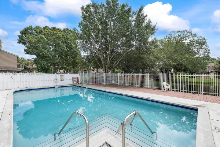 Swimming pool featuring a concrete deck, metal railings, and a white privacy fence