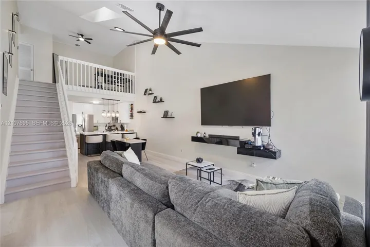 Vaulted ceilings featuring a skylight, multi-blade ceiling fan, and vinyl staircase with white railings