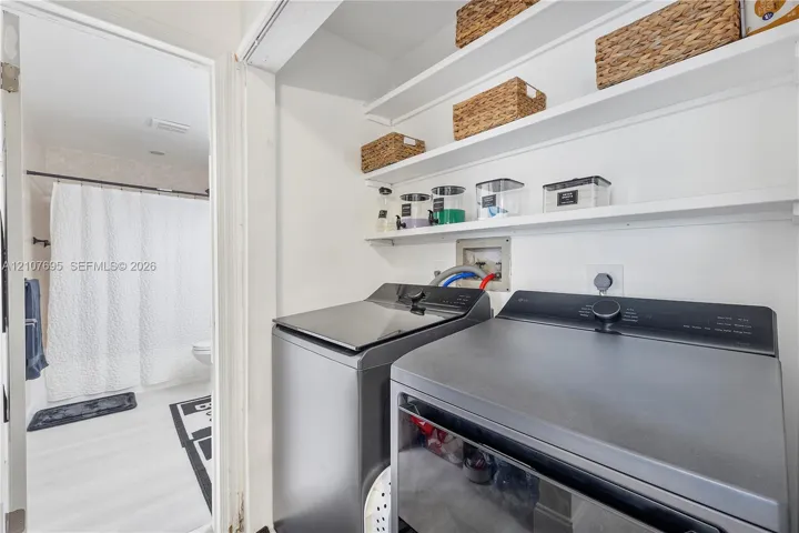 Laundry area featuring built-in shelving, white walls, and wood-finish flooring