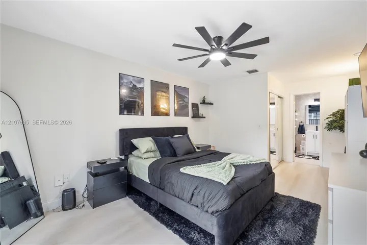 Neutral-toned interior space featuring wood-finish flooring, a multi-blade ceiling fan with integrated lighting, and dual wall-mounted floating shelves