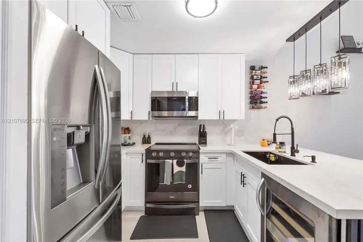 Kitchen featuring white shaker-style cabinetry, white countertops with grey veining, stainless steel appliances, a black undermount sink with a gooseneck faucet, and multi-pendant overhead lighting
