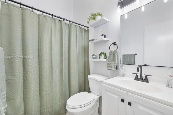 Bathroom featuring a white vanity with a rectangular sink, matte black faucet, wall-mounted light fixture with glass shades, frameless mirror, and built-in shelving