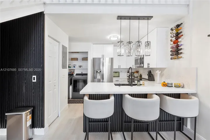 Kitchen featuring white cabinetry, a quartz-topped island with vertical slat detailing, stainless steel appliances, a modern multi-pendant light fixture, and a built-in wall-mounted wine rack